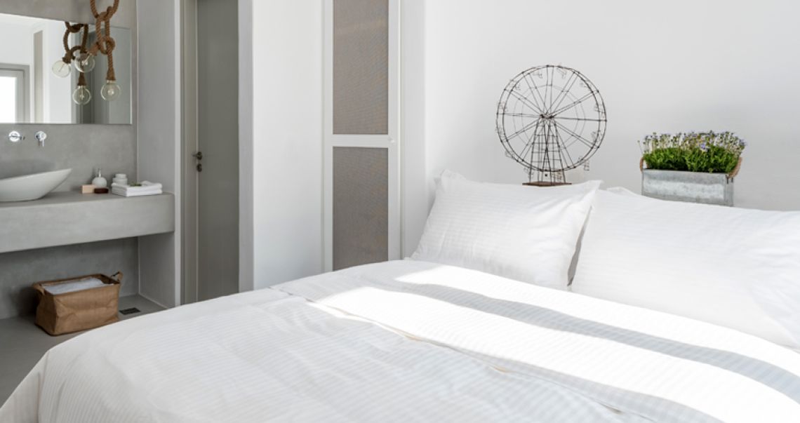 Modern bedroom suite featuring a white bed with unique wire art decor, leading into an open-plan grey bathroom area with a vessel sink.