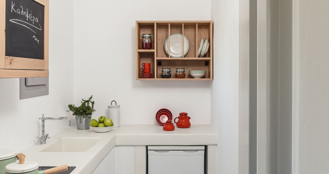 Modern white kitchenette featuring a farmhouse sink, open wooden shelving with dishware, and a chalkboard cabinet door.