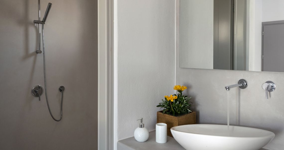 Modern grey microcement bathroom vanity featuring a white vessel sink, chrome fixtures, and a wooden planter with yellow flowers.
