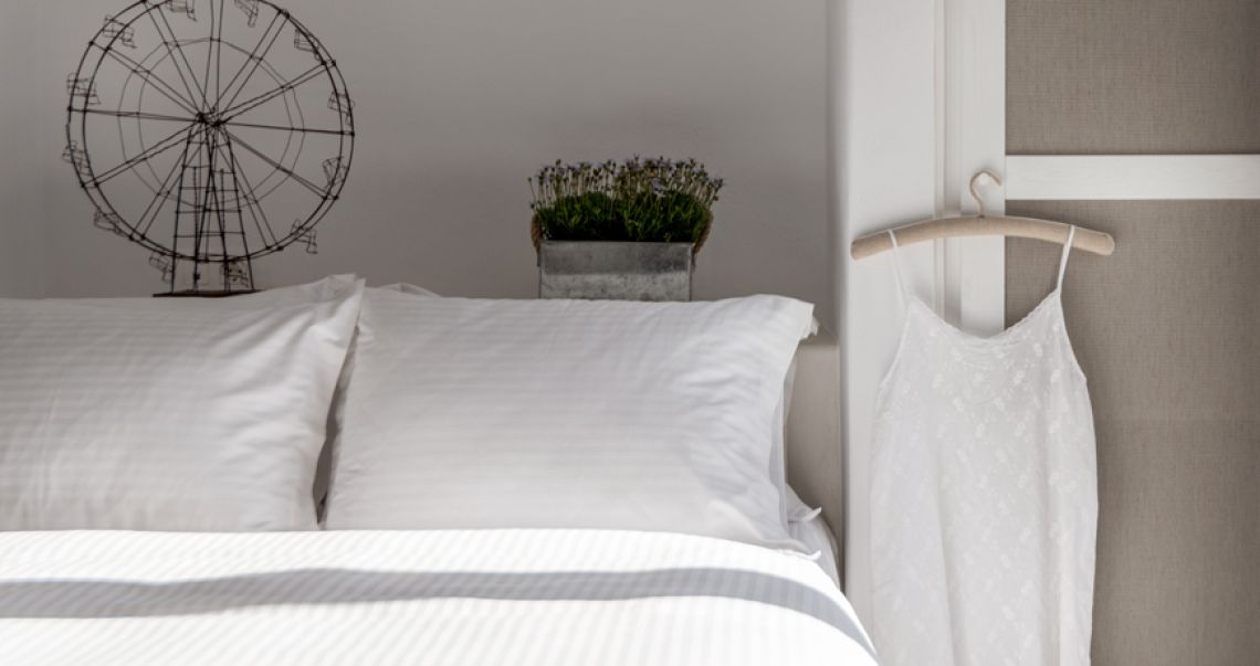 Close-up of bedroom decor featuring a wire Ferris wheel sculpture and fresh flowers on the headboard, with a white nightgown hanging on the wardrobe.