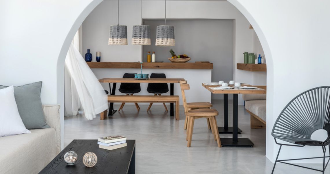 Open-plan dining and living space featuring Cycladic white arches, woven pendant lights, and modern wooden furniture.