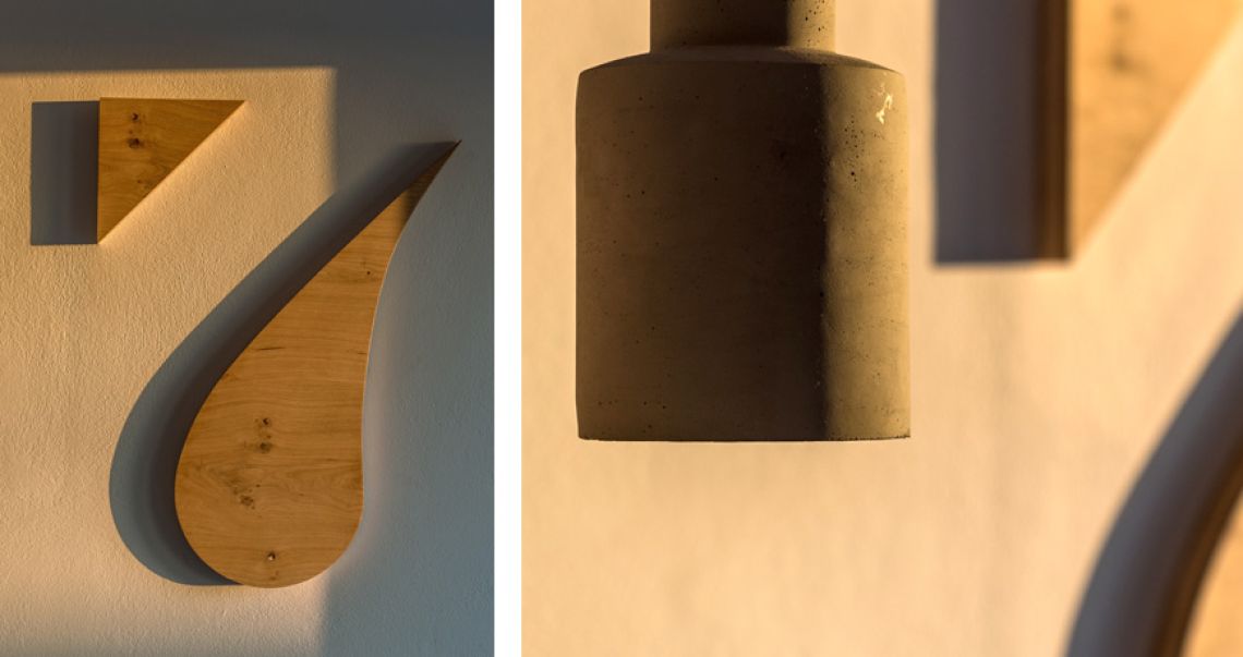 Detail shot highlighting abstract wooden wall art on the left and a minimalist concrete pendant lamp on the right.