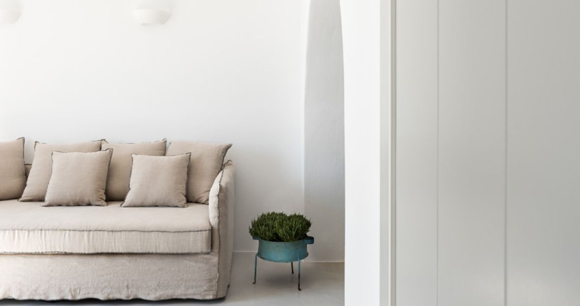 Minimalist white living space featuring a comfortable beige linen sofa with scatter pillows and a rustic blue metal planter.