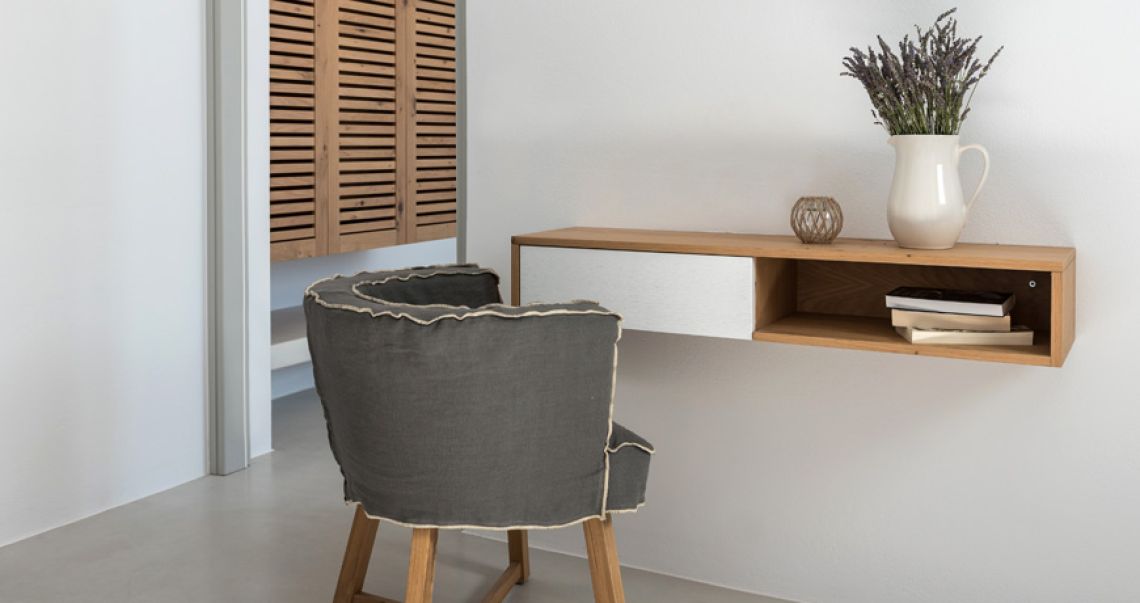 Stylish workspace featuring a floating wooden desk, a grey linen chair, and a white pitcher filled with dried lavender.