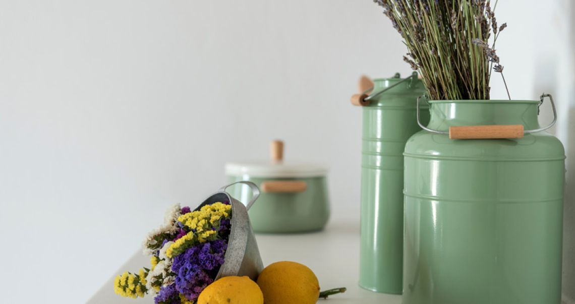 Kitchen decor detail featuring vintage-style sage green canisters filled with dried herbs and a metal bucket of fresh colorful flowers.