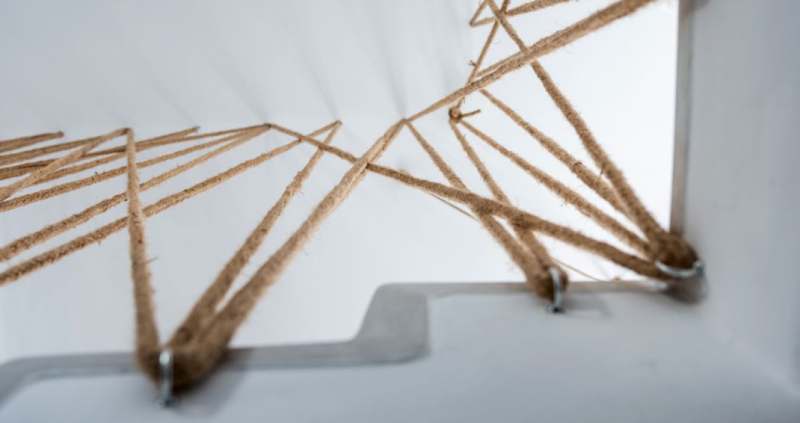 Low-angle artistic view of a crisscrossed rope railing installation attached to white architectural beams.